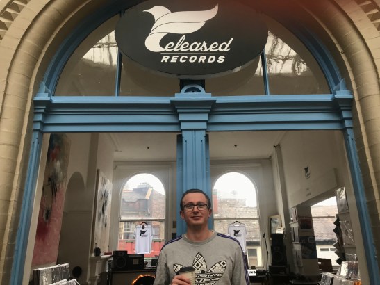 A landscape image of a man - Liam McIntyre - outside Released Records, an record store