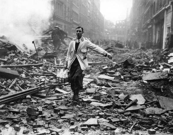 Black and white image of a milkman delivering milk through the rubble and ruins of London in World War Two